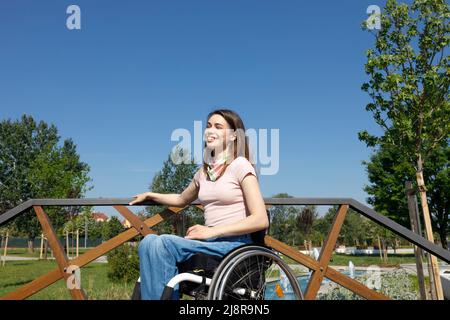 Una donna sorridente, godendo e apprezzando una piacevole giornata estiva da sola sulla sua sedia a rotelle Foto Stock