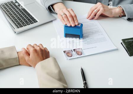 Primo piano medio di un ufficiale consolare irriconoscibile che appone il sigillo di approvazione sul modulo di richiesta del visto per la donna musulmana dopo l'intervista Foto Stock