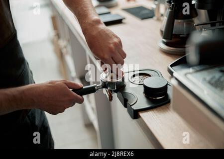 Il primo piano delle mani del barista uomo sta tenendo il portafiltro e la manomissione del caffè Foto Stock