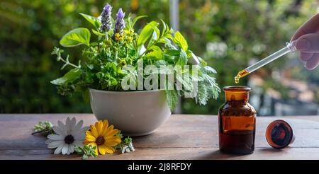 Medicina alternativa di salute. Goccia d'olio essenziale che cade in una bottiglia di vetro, primo piano. Cosmetici naturali, siero e vitamine. Erbe fresche in un mortaio sopra Foto Stock