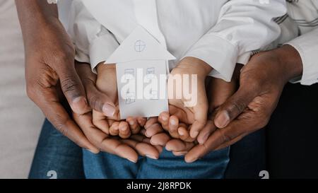 Primo piano femmina maschio e bambino mani di famiglia africana tenendo forma di cartone di casa immagine di casa sogno di alloggio ricollocazione appartamento nuovo m Foto Stock