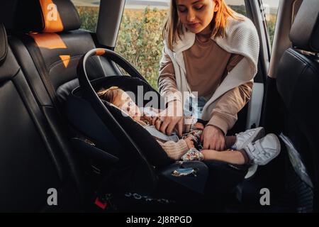 La giovane madre mette la sua figlia del bambino in un seggiolino dell'automobile del bambino nell'automobile Foto Stock