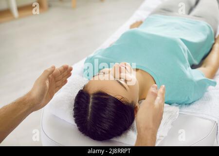 La donna viene sottoposta a terapia alternativa durante la sessione di reiki nella moderna sala massaggi. Foto Stock