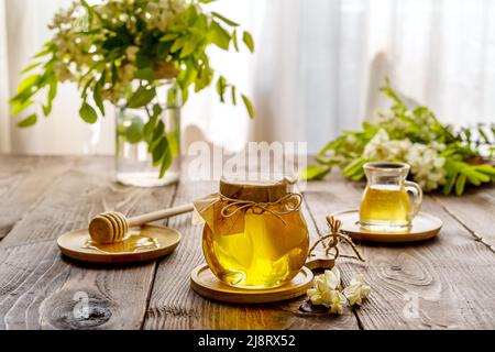 Miele di acacia in vaso di vetro con cucchiaia di legno e fiori a parte su sfondo di legno Foto Stock