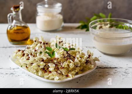 Fiori di acacia su piatto con ingredienti per cucinare frittelle di Acacia con pastella e ingredienti principali per cucinare a parte Foto Stock
