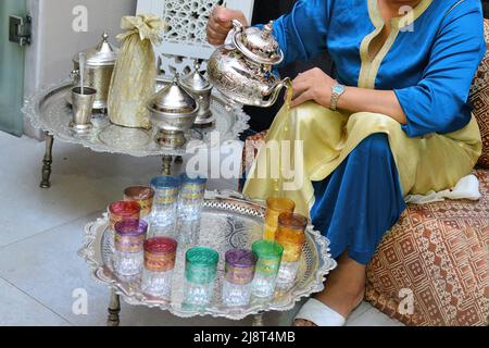 Arab Woman che versa il tè. Donna araba del Medio Oriente in abito tradizionale marocchino che beve tè marocchino. Ramadan tema di vacanza. Foto Stock