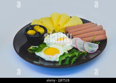 Un piatto di uova, formaggio, fette di tacchino e olive su sfondo bianco. Colazione al ristorante Foto Stock