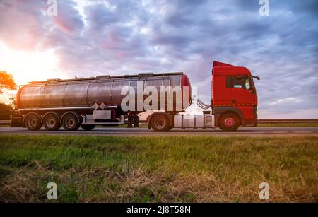 Un moderno camion con una petroliera semi-rimorchio trasporta merci pericolose sullo sfondo di un tramonto in estate. Trasporto di carichi liquidi Foto Stock