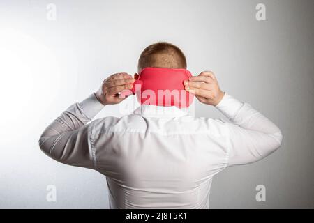 Un uomo tiene un cuscinetto riscaldante con acqua calda sul retro della testa. Rilassamento muscolare e vasodilatazione della testa, termoterapia. Trattamento del mal di testa Foto Stock