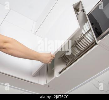 Un uomo apre la porta della facciata della cucina con un meccanismo di sollevamento. Cucina moderna Foto Stock