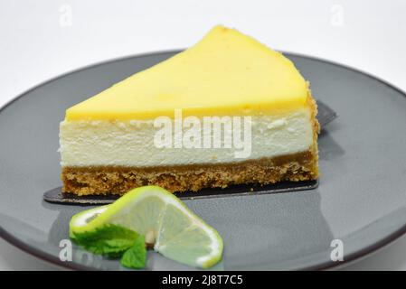 Fetta di Cheesecake al limone su piatto grigio su sfondo bianco Foto Stock
