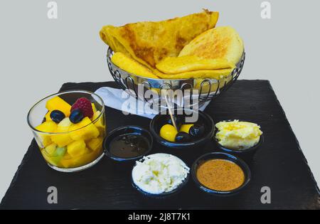 Colazione marocchina su marmo nero con sfondo bianco, dolci con marmellata, burro, olive e Macedonia di frutta Foto Stock