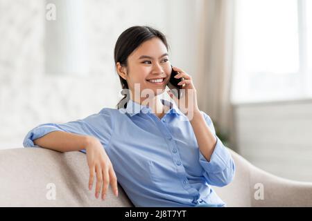 Allegra donna asiatica che parla sullo smartphone a casa Foto Stock