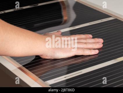 Un uomo controlla con la mano il calore del riscaldamento a infrarossi del pavimento dopo l'installazione Foto Stock