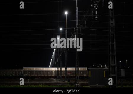 Stazione di trasporto di notte a Zurigo, Spreitenbach. I treni merci sono illuminati da fari luminosi. L'immagine è scura in primo piano. Foto Stock