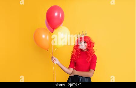 bambino allegro in corona con palloncino di elio su sfondo giallo Foto Stock