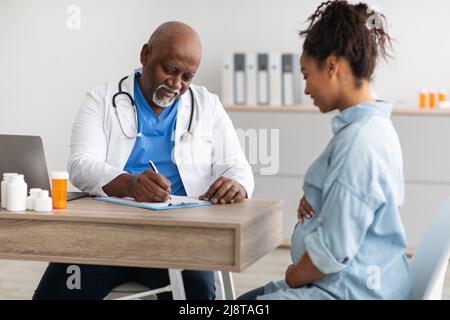 Medico di sesso maschile consulenza giovane donna incinta sorridente, scrittura record Foto Stock