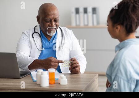 Medico nero esperto che mostra pillole a paziente femminile Foto Stock