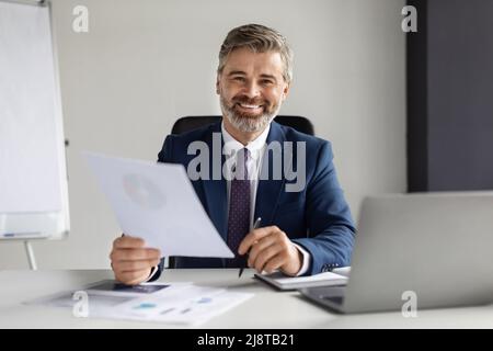 Uomo d'affari maturo in tuta che lavora con documenti alla scrivania in ufficio Foto Stock