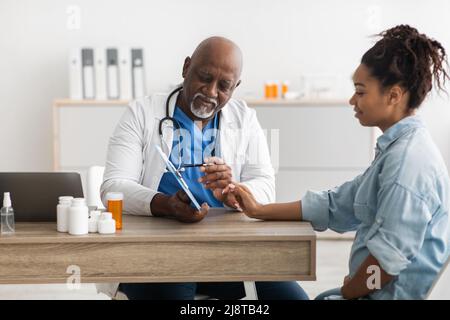 Medico esperto di colore che spiega il piano di trattamento alla paziente femminile Foto Stock