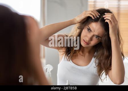 Signora infelice cercando fiocchi di capelli che hanno forfora in piedi in bagno Foto Stock