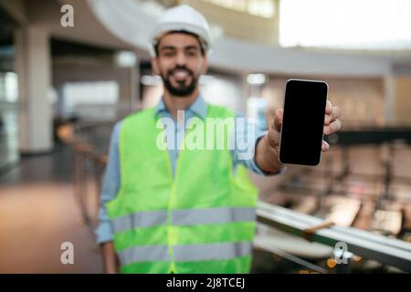 Felice uomo musulmano attraente millenario ingegnere con barba in casco e uniforme protettiva Foto Stock