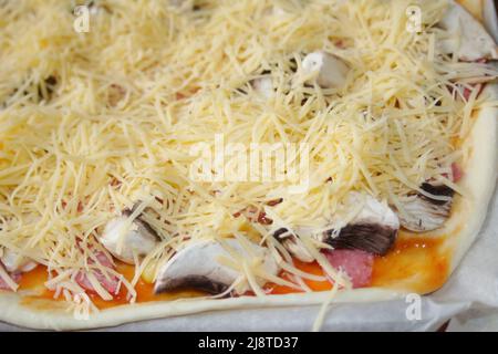 Defocalizzare in primo piano la pizza intera con mozzarella grattugiata. Defocalizzare gli ingredienti sfocati per la pizza sull'impasto. Spazio di copia. Cucina italiana b Foto Stock