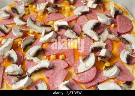 Defocalizzare gli ingredienti del primo piano per la pizza sull'impasto. Salsa di pomodoro rosso, salsicce, mais dolce. Pizza italiana fatta in casa. Base di Margarita. Home culinario. Superiore Foto Stock