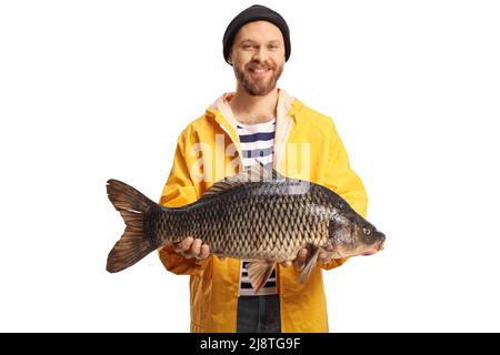 Giovane pescatore in un impermeabile giallo che tiene un grosso pesce carpa e sorride isolato su sfondo bianco Foto Stock
