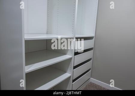 Vista di alti armadi e cassetti bianchi all'interno di una stretta passeggiata in armadio all'interno di una camera da letto principale Foto Stock