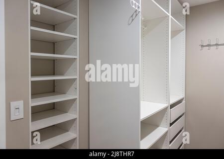 Vista di alti armadi e cassetti bianchi all'interno di una stretta passeggiata in armadio all'interno di una camera da letto principale Foto Stock