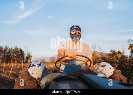 Uomo contadino con la maschera peste sopra, guidando un vecchio trattore nel mezzo della sua campagna. Foto Stock