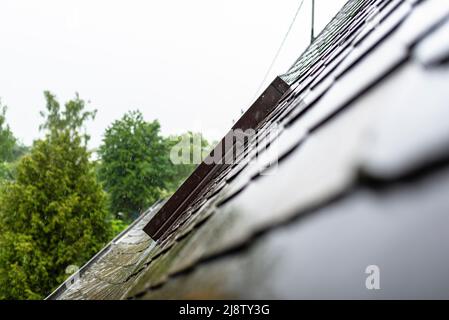 Forte pioggia che cade sul tetto che trabocca la grondaia con acqua in caso di pioggia, vetro del tetto visibile. Foto Stock