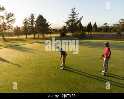 Vista aerea del giovane afro-americano guardando l'amico caucasico che prende il tiro di golf a corso Foto Stock