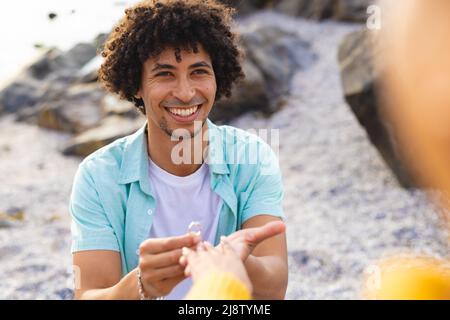 Allegro afroamericano uomo mettere anello di fidanzamento nel dito della ragazza alla spiaggia Foto Stock