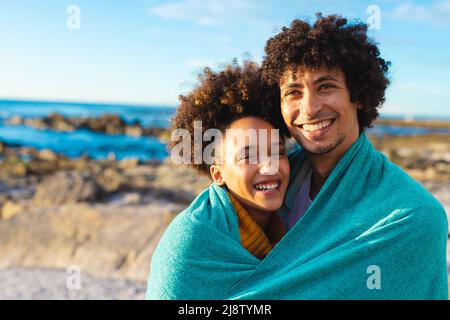Ritratto di amorevole allegra afro americano giovane coppia avvolto in coperta alla spiaggia Foto Stock