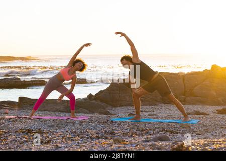 Giovane coppia afroamericana che si piega lateralmente mentre si fa yoga in spiaggia durante il tramonto, spazio copia Foto Stock