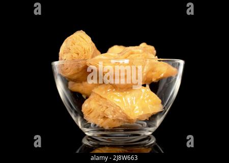 Diverse fette di dolce baklava al miele in una ciotola di vetro, primo piano, isolato su sfondo nero. Foto Stock