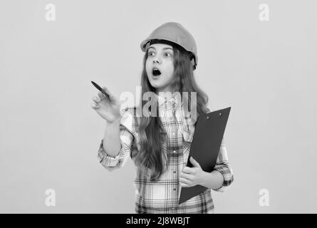 scioccata ragazza teen in casco e camicia a scacchi facendo appunti sulla clipboard, lavorando Foto Stock