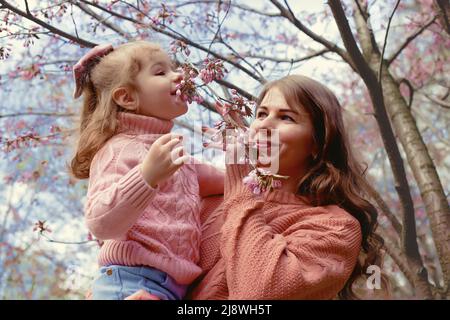 Madre e bambina, in piedi nel parco sotto un ciliegio fiorito Foto Stock