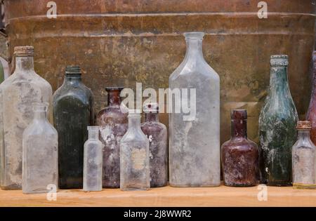 Primo piano di vecchie bottiglie di vetro di liquore e medicina non interrate contro un fondo di bidone di metallo arrugginito. Foto Stock