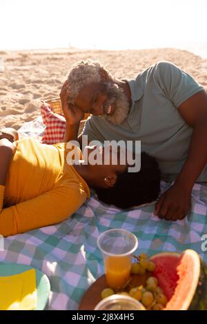 Romantica coppia afro-americana felice che si guarda mentre si trova su coperta in spiaggia Foto Stock