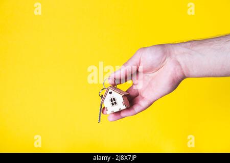 Acquisto di una casa. L'acquirente riceve la chiave per la proprietà. Appartamento ipotecario. Chiavi e una piccola casa in legno in mano. Consegna delle chiavi all'Ora Foto Stock