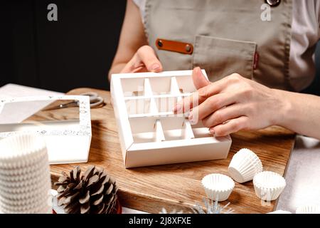 Una donna fa scatole di caramelle fatte a mano. Primo piano delle mani femminili. Foto Stock