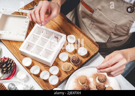 Donna confettatrice fare a mano pregiato tartufo al cioccolato. Primo piano di mani femminili e deliziosi cioccolatini. Caramelle fatte a mano. Vista dall'alto Foto Stock