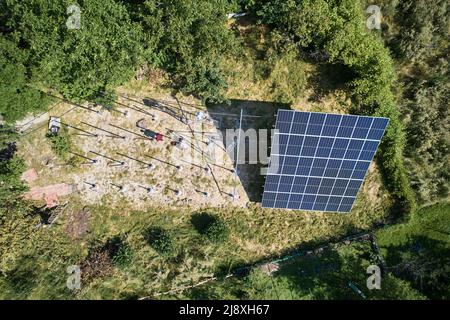 Vista aerea dei lavoratori che installano pannelli solari su un'alta piattaforma in acciaio in campo in giornata di sole. Concetto di energia alternativa. Foto Stock