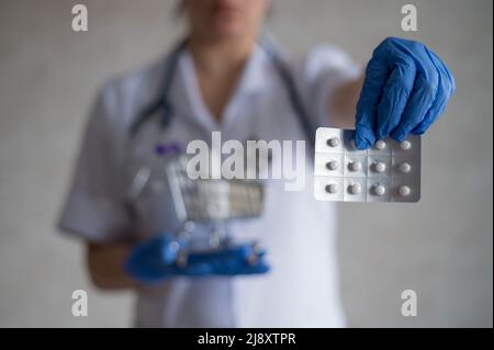 Un medico senza volto in guanti di gomma mostra un blister con pillole e contiene un mini carrello con una confezione completa di diversi farmaci Foto Stock