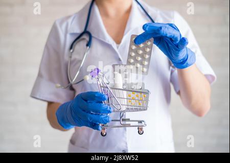 Medico senza volto in guanti di gomma mette un blister con compresse. Un mini carrello per lo shopping. Il concetto di acquistare la medicina in farmacia. Farmaco Foto Stock