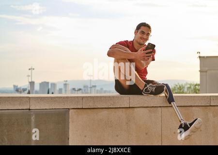 Uomo con disabilità utilizzando il suo cellulare e sorridendo mentre si rilassa all'aperto. Foto Stock