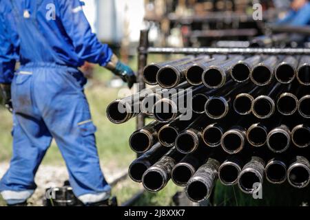 Tubi di perforazione per carro di perforazione impilati con i lavoratori dell'industria petrolifera in background. Industria petrolifera e del gas. Martinetto della pompa dell'olio grezzo su un campo petrolifero. Perforazione di olio AN Foto Stock